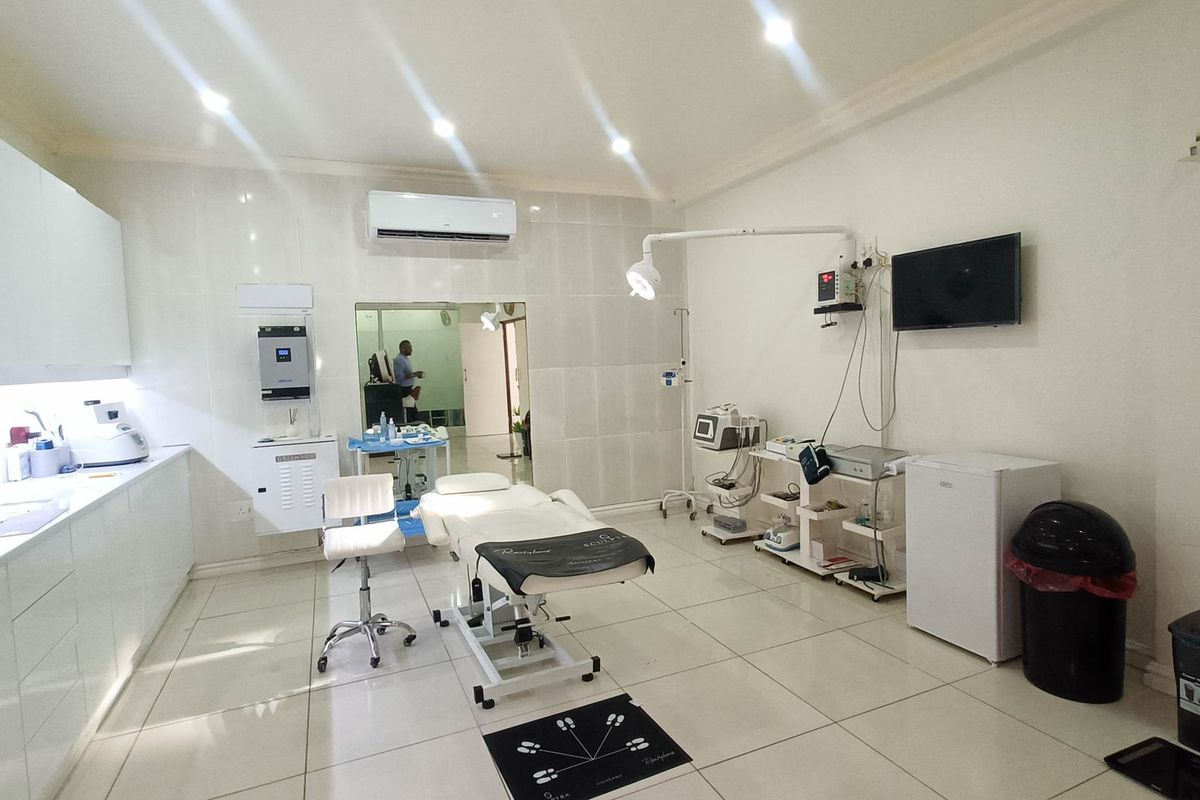 A well-maintained commercial treatment room featuring tiled flooring, built-in cabinetry, wall-mounted air conditioning, and professional medical examination lighting.