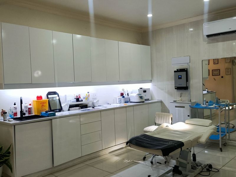A well-maintained clinical utility space featuring extensive built-in cabinetry, integrated sink, tiled flooring, and wall-mounted air conditioning, suitable for medical or aesthetic practice.