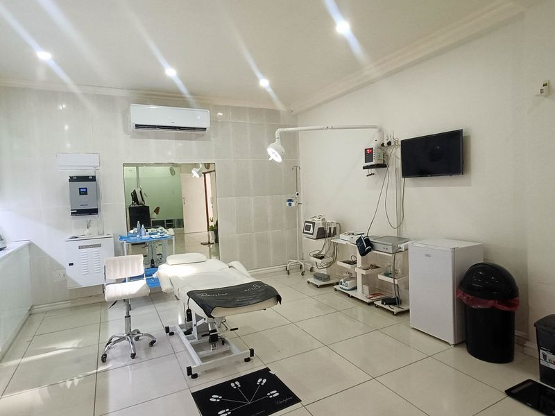 A well-maintained clinical treatment room featuring tiled flooring, built-in cabinetry, wall-mounted air conditioning, and professional medical lighting fixtures.