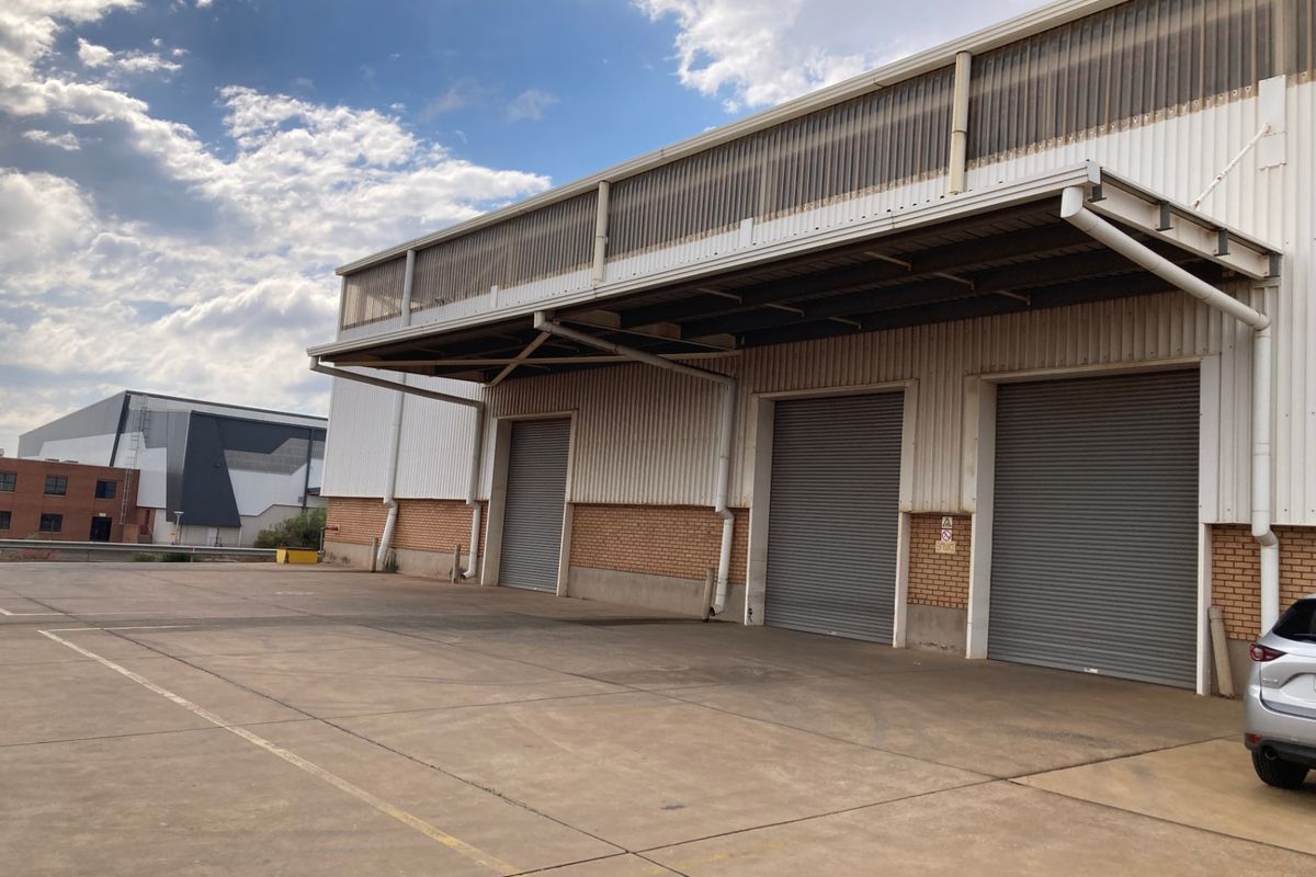 Industrial warehouse exterior featuring a large concrete loading yard, three roller shutter doors, and a covered loading canopy.