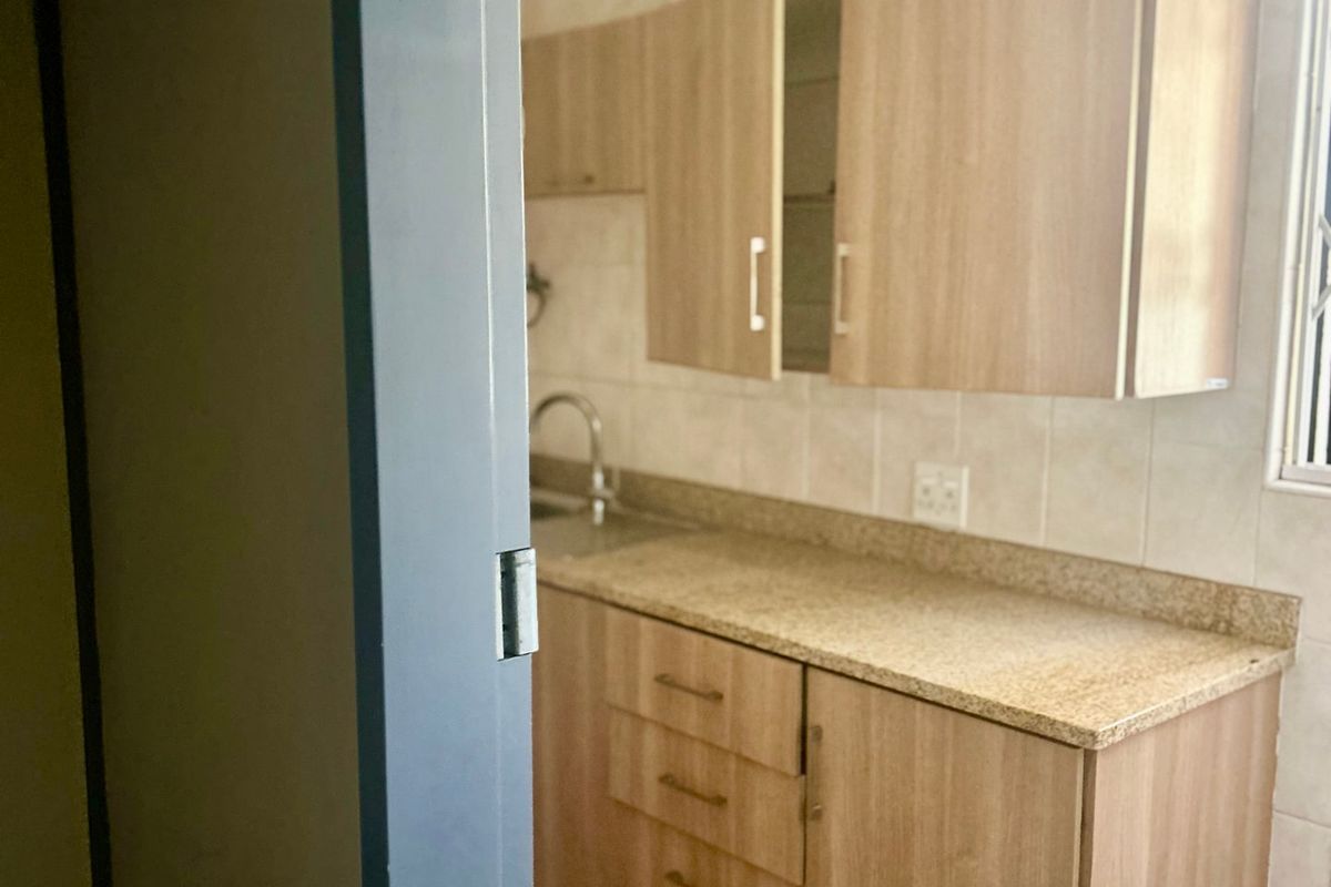 A compact kitchen featuring light wood-tone cabinetry, granite countertops, a stainless steel sink, and neutral tiled finishes.