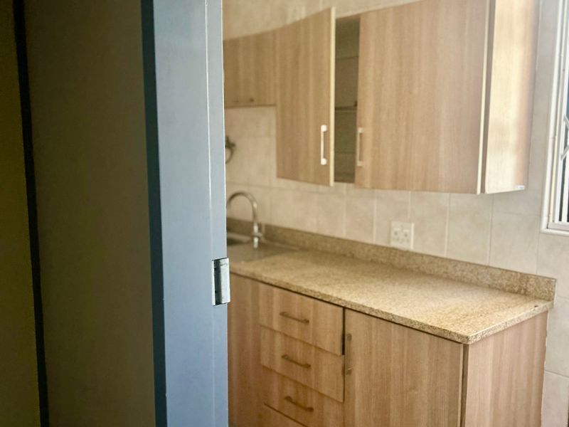 A compact kitchen featuring light wood-tone cabinetry, granite countertops, a stainless steel sink, and neutral tiled finishes.