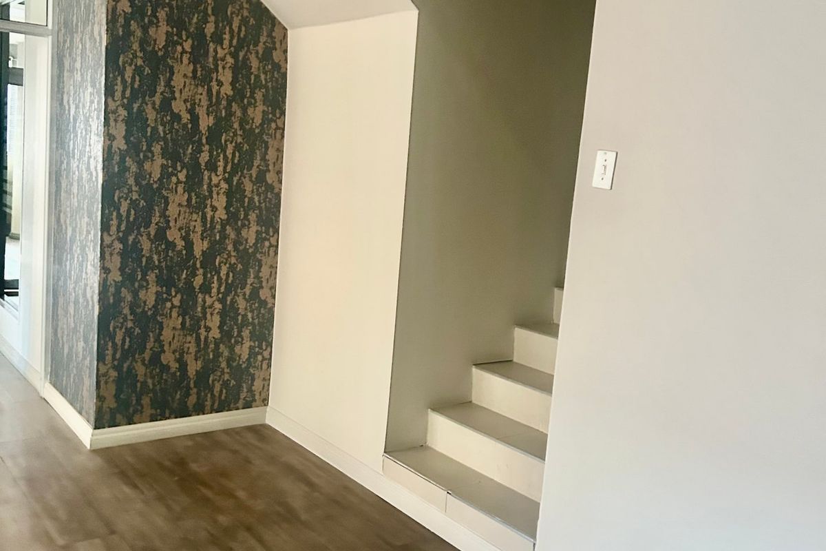 A clean, modern hallway featuring laminate flooring, a staircase, and a wall-mounted air conditioning unit.