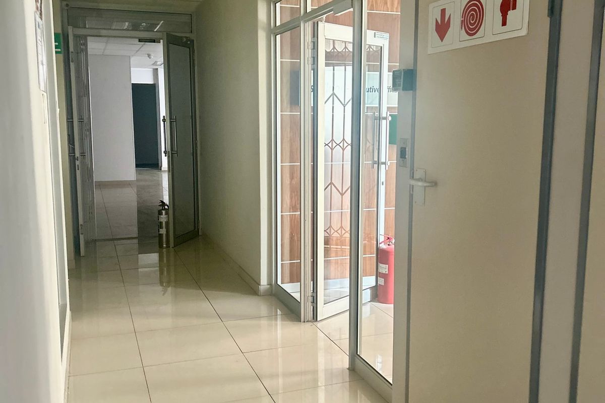 A clean, functional commercial hallway featuring tiled flooring, suspended ceilings, and glass-paneled office doors with integrated fire safety signage.