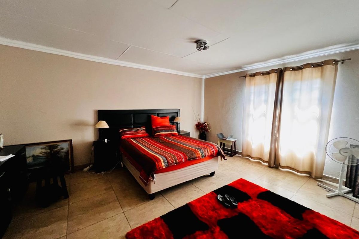 A spacious bedroom featuring neutral wall tones, tiled flooring, and large windows with curtain fittings, offering a functional and well-lit living space.