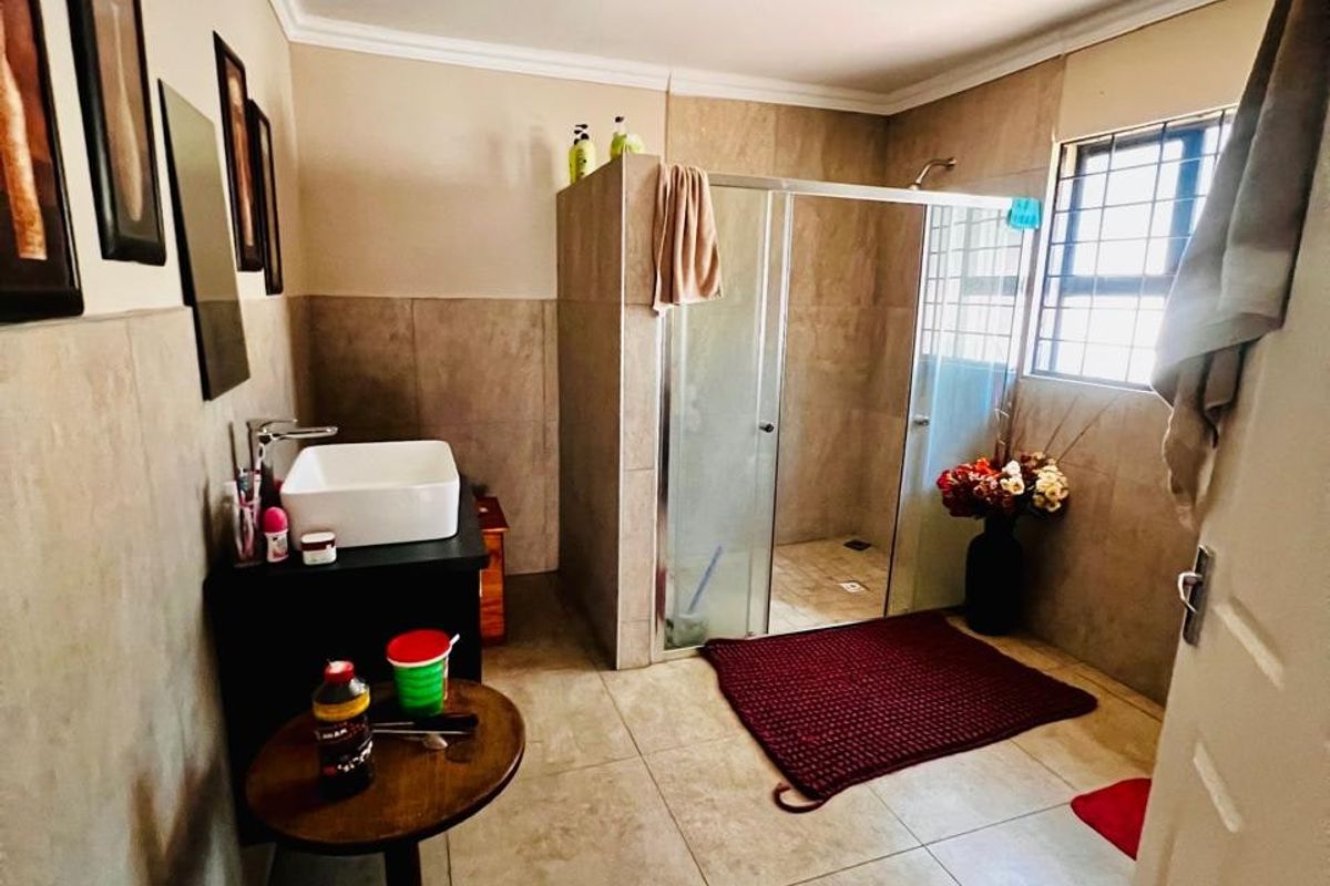 A functional bathroom featuring a glass-enclosed shower, vessel sink vanity, and neutral wall and floor tiling.