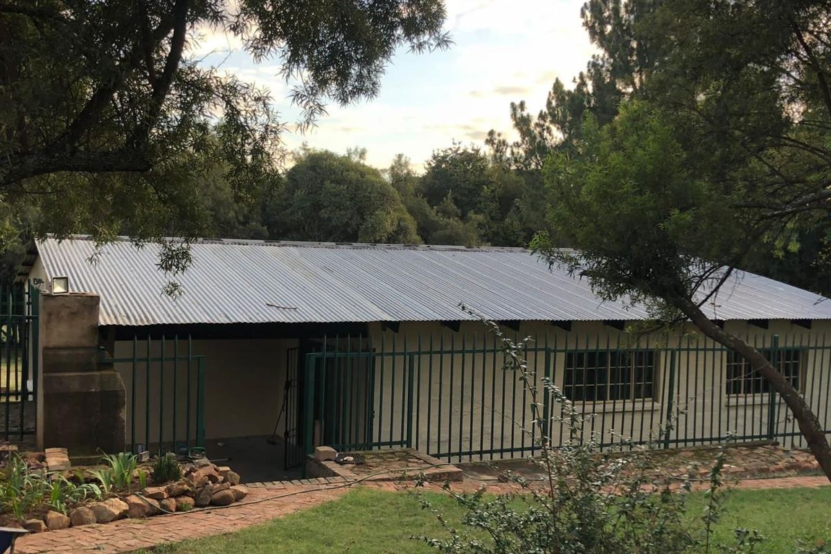 Rear view of a commercial building featuring a corrugated metal roof, brick chimney, and secure perimeter fencing set within a landscaped garden area.