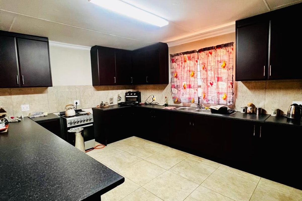 A functional kitchen featuring dark cabinetry, laminate countertops, a freestanding stove, and tiled flooring with a neutral backsplash.