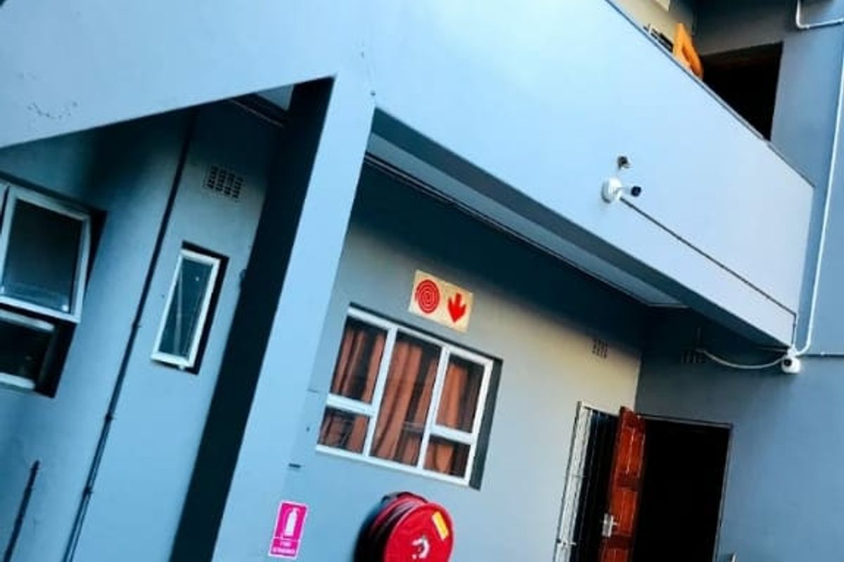 Exterior view of a multi-story commercial building featuring a balcony, staircase, and essential fire safety equipment including a hose reel and extinguisher.