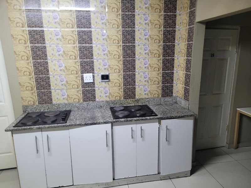 A compact kitchen area featuring granite countertops, dual built-in electric hobs, white cabinetry, and decorative patterned wall tiling.