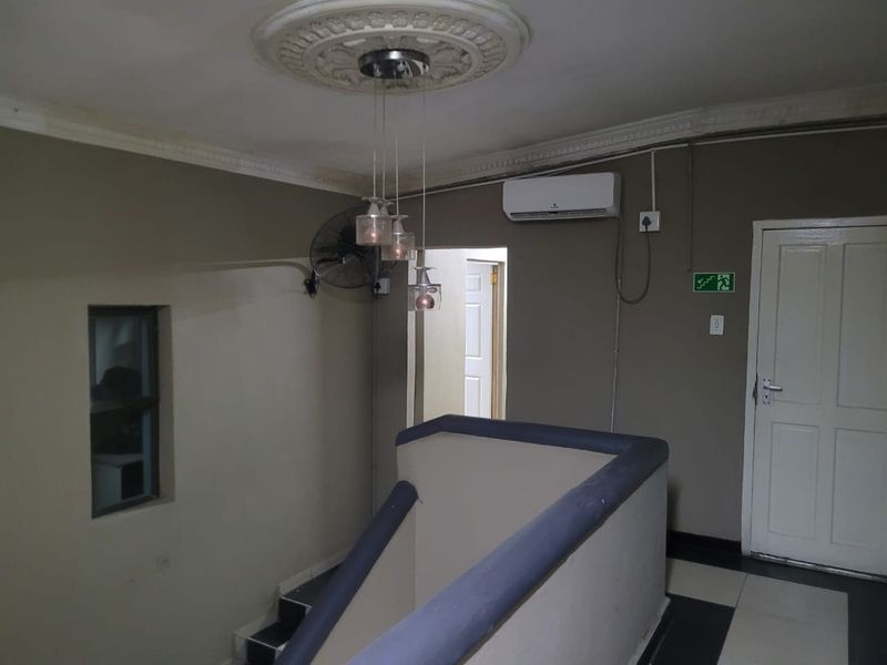 A commercial hallway featuring a staircase with a balustrade, ceiling rose, pendant lighting, and wall-mounted air conditioning unit.