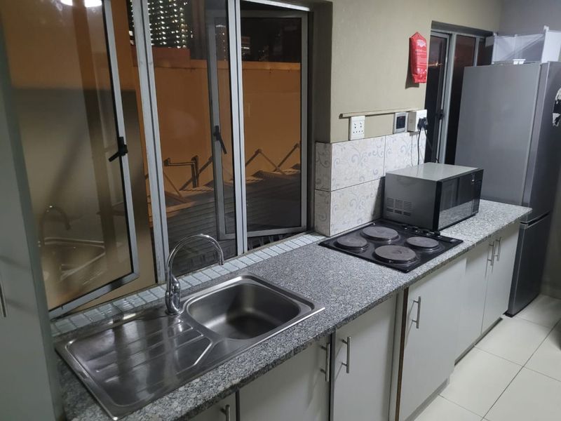 A functional kitchen area featuring granite countertops, a stainless steel sink, an electric hob, and built-in cabinetry with tiled backsplash.