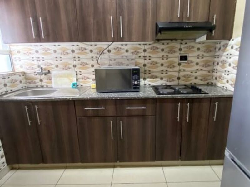 Compact kitchen featuring dark wood-finish cabinetry, granite countertops, a built-in hob with extractor fan, and tiled flooring.