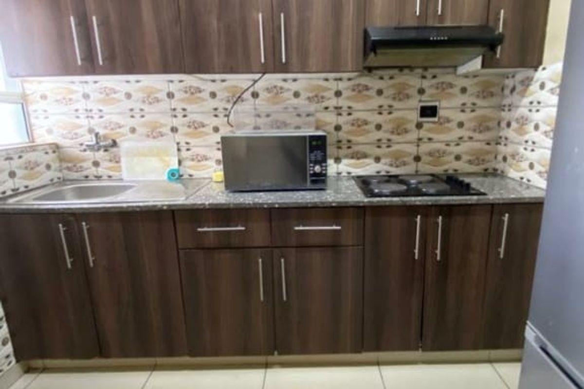 Compact kitchen featuring dark wood-finish cabinetry, granite countertops, a built-in hob with extractor fan, and tiled flooring.