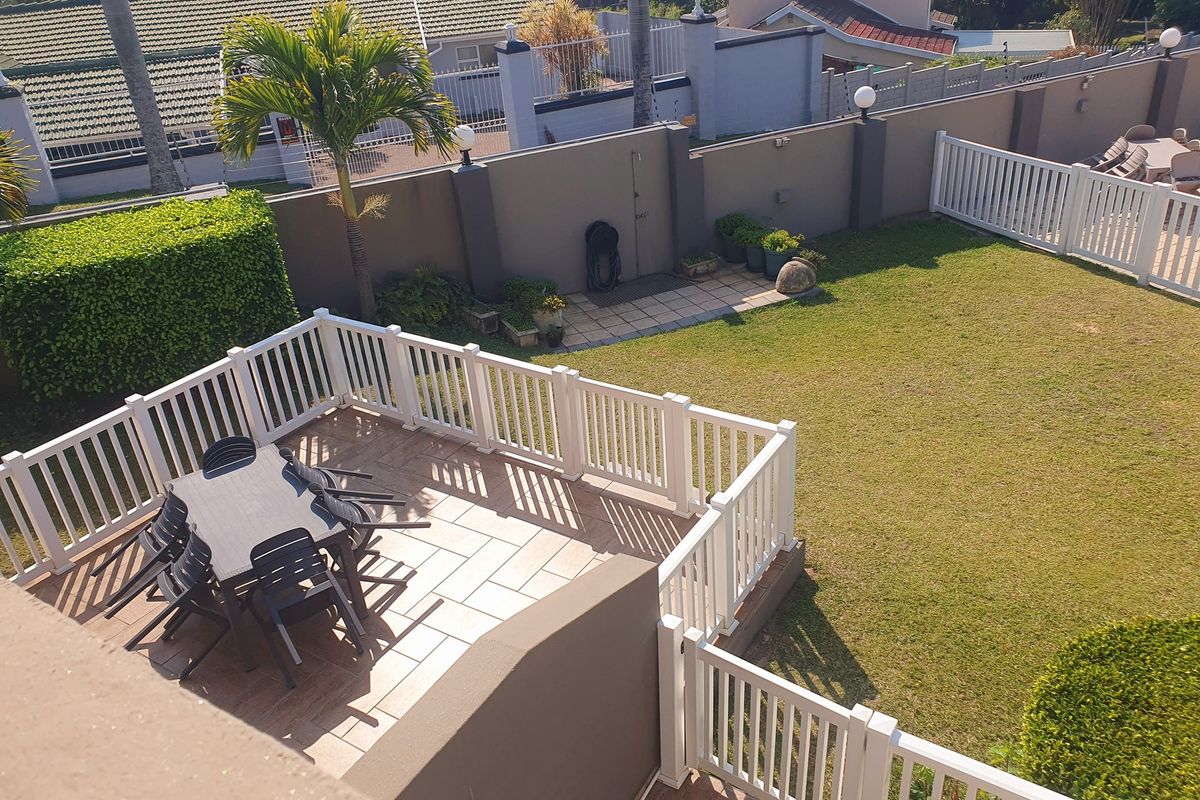 Elevated view of a well-maintained rear garden featuring a paved patio area, white picket fencing, and a manicured lawn.