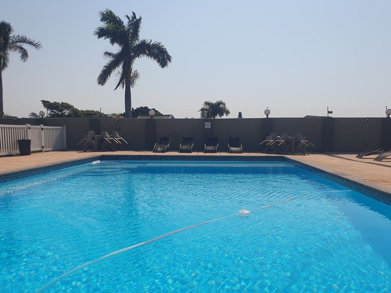 A well-maintained outdoor swimming pool area featuring a paved deck, perimeter boundary wall, and white picket fencing.