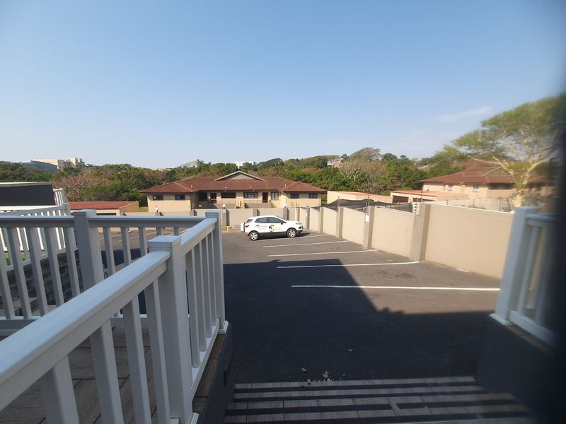 View of the property's paved parking area and driveway, featuring boundary walls with electric fencing and a white balustrade entrance.