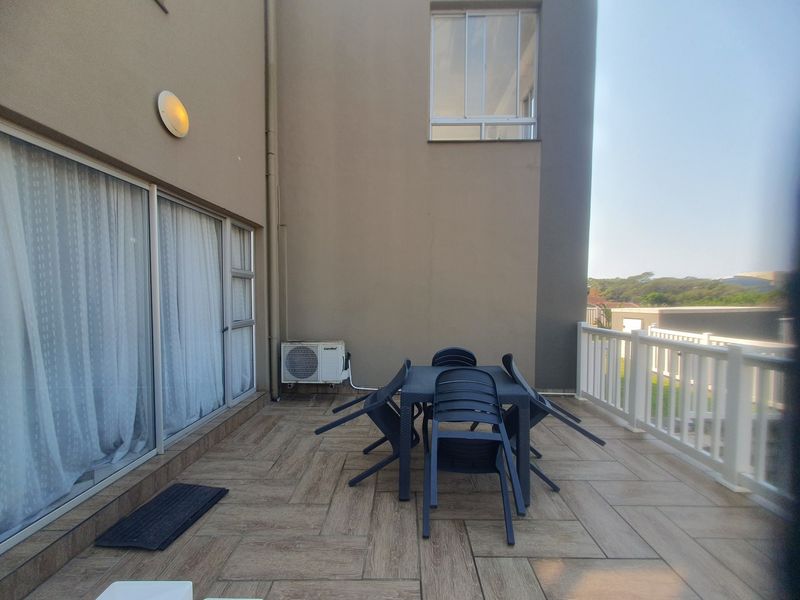 A spacious balcony featuring wood-look tiled flooring, a white balustrade, and sliding glass door access to the interior living area.