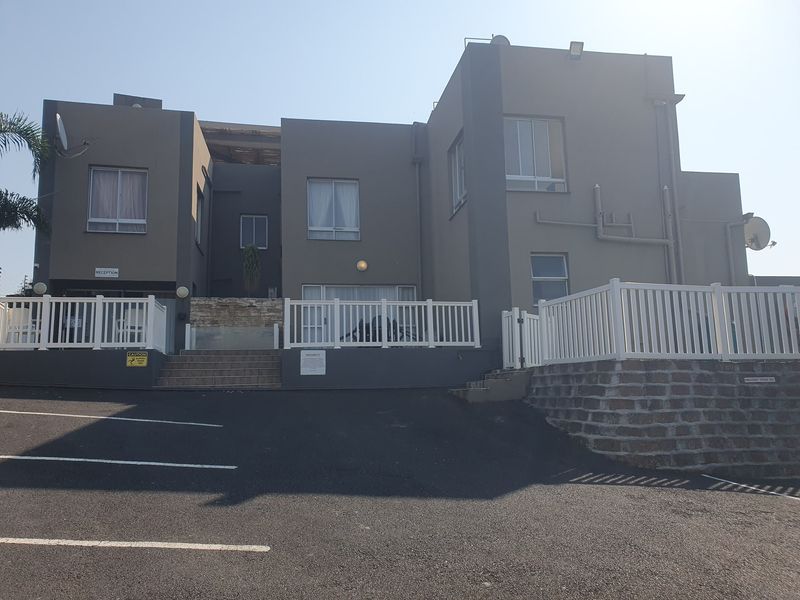 Front elevation of a multi-level residential building featuring a paved driveway, white perimeter fencing, and stone retaining wall elements.