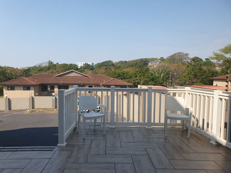An elevated balcony featuring a white balustrade and modern wood-look tiled flooring, offering an open outdoor space with neighbourhood views.
