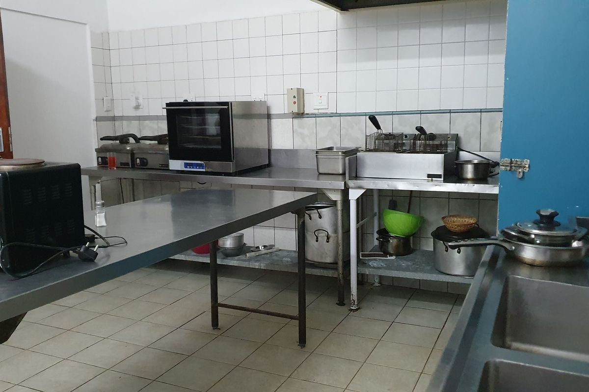 Commercial kitchen space featuring stainless steel work surfaces, tiled walls, and industrial-grade food preparation equipment.