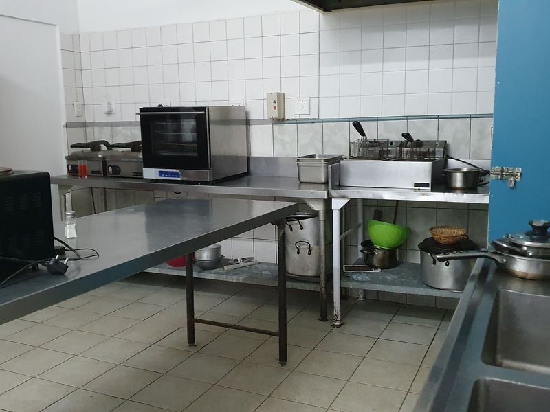 Commercial kitchen space featuring stainless steel work surfaces, tiled walls, and industrial-grade food preparation equipment.