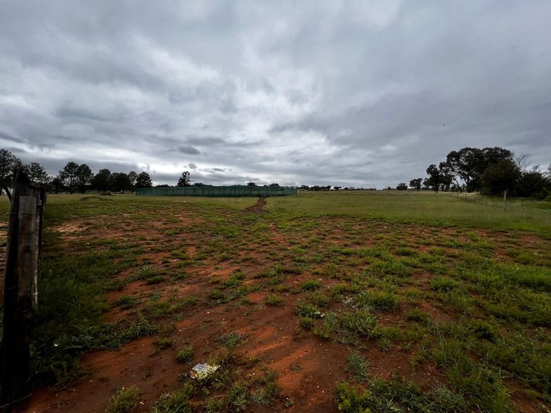 Expansive undeveloped commercial land featuring natural terrain, perimeter wire fencing, and distant netting structures under an overcast sky.