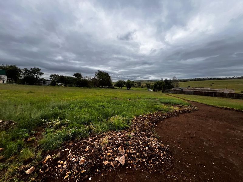 An expansive open plot of land featuring a dirt access road and perimeter fencing, set against a rural landscape under a cloudy sky.