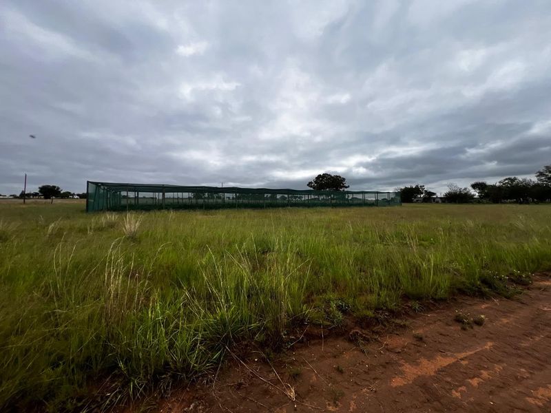 Expansive open land featuring a large agricultural netting structure, suitable for commercial farming or cultivation purposes.