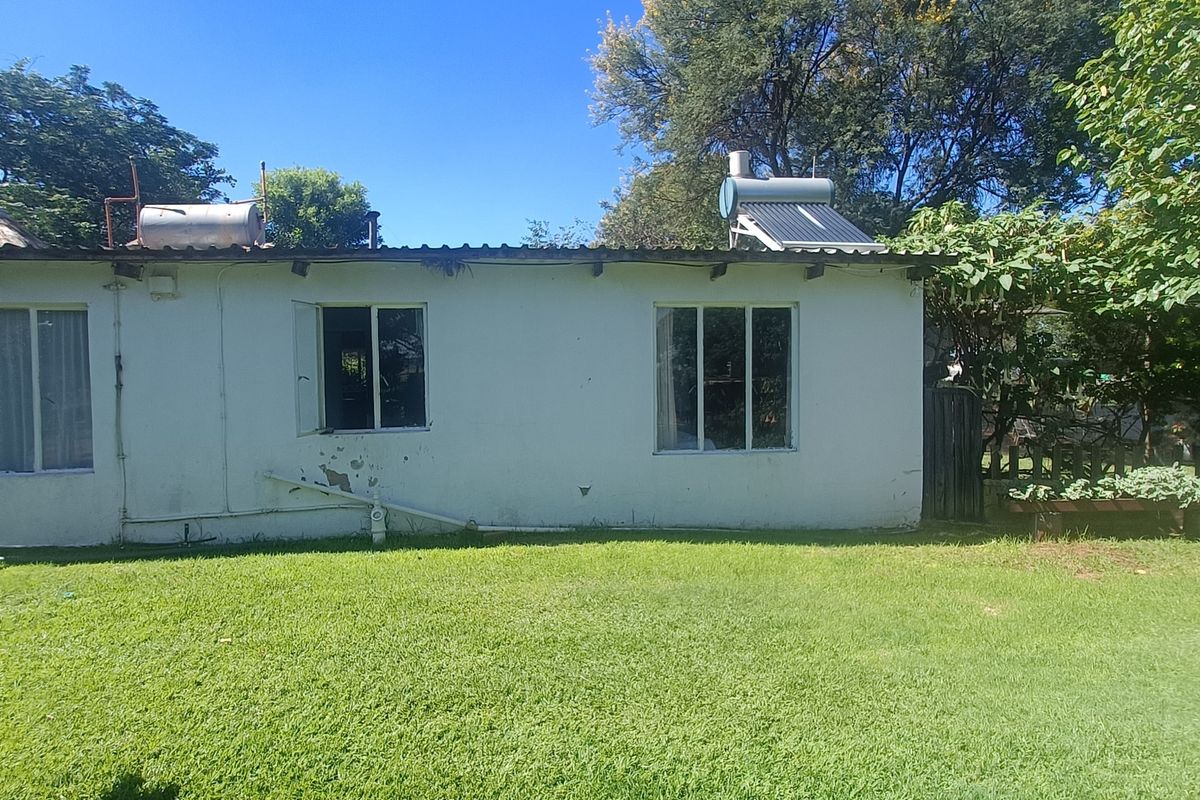 Rear view of the farm dwelling featuring a lawn, solar water heating system, and exterior wall finishes requiring maintenance.