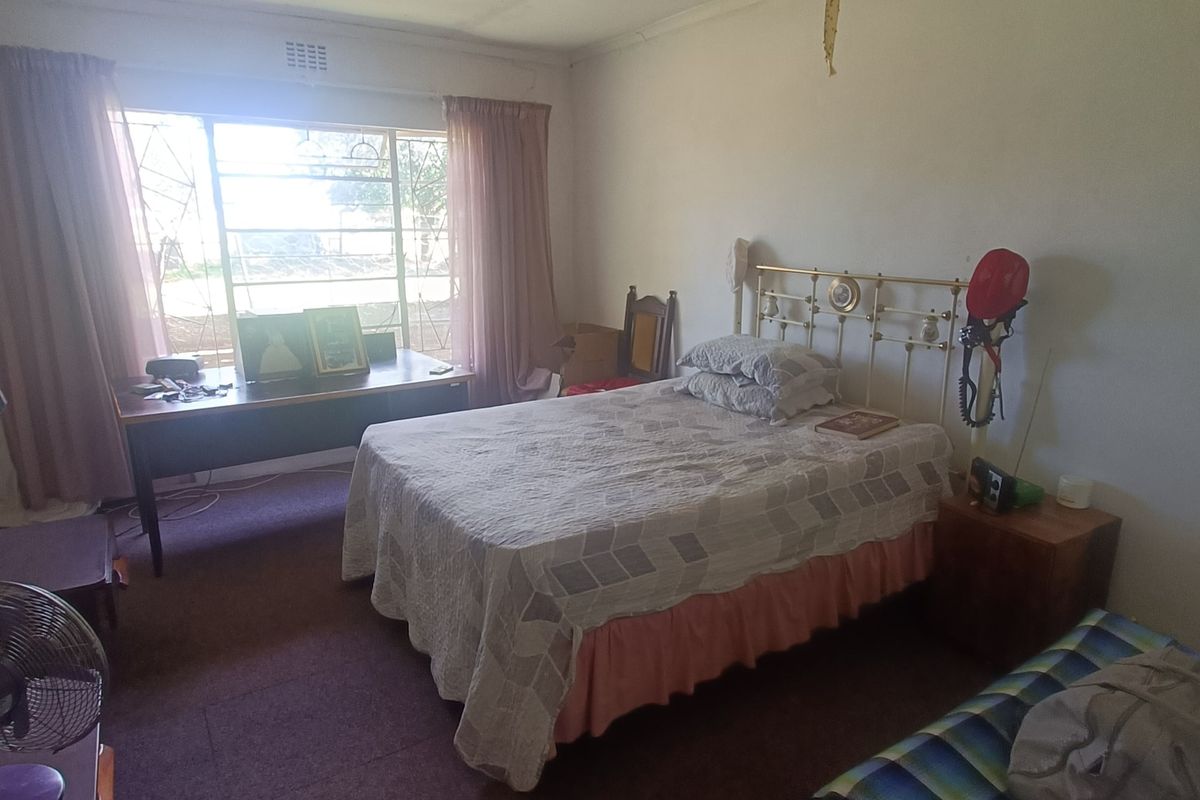 A bedroom featuring a metal window frame and carpet flooring, showing signs of wear and ceiling damage requiring maintenance.