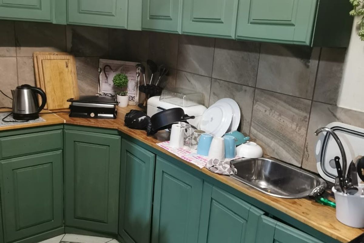 A functional kitchen featuring green shaker-style cabinetry, wooden countertops, a stainless steel sink, and a tiled backsplash with mosaic flooring.