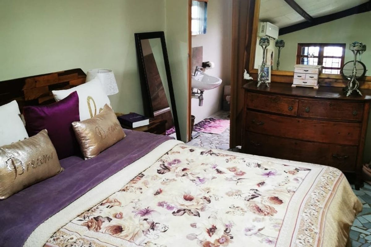 A bedroom featuring exposed timber ceiling beams and tiled flooring, with direct access to an en-suite bathroom.