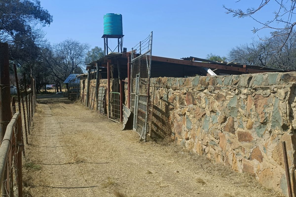 Exterior view of a farm utility area featuring a stone wall, wire fencing, and a raised water tank with a weathered metal roof structure.