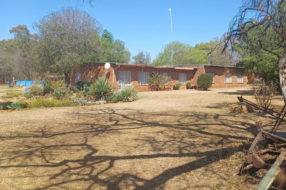 A view of the farm property featuring a single-story brick dwelling set within a large, open garden area with mature trees.