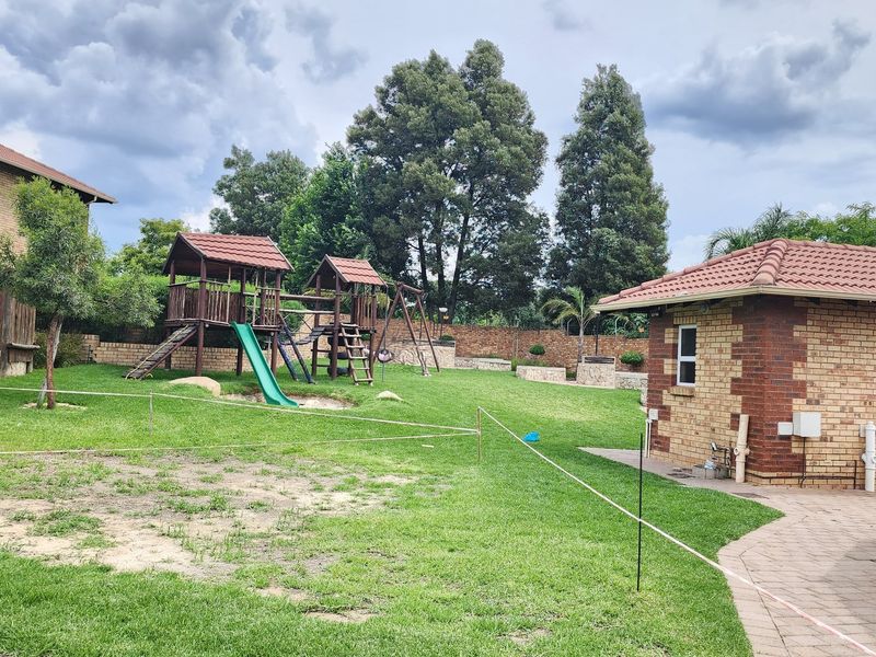A spacious residential garden featuring a well-maintained lawn, a brick outbuilding with a tiled roof, and a paved walkway.