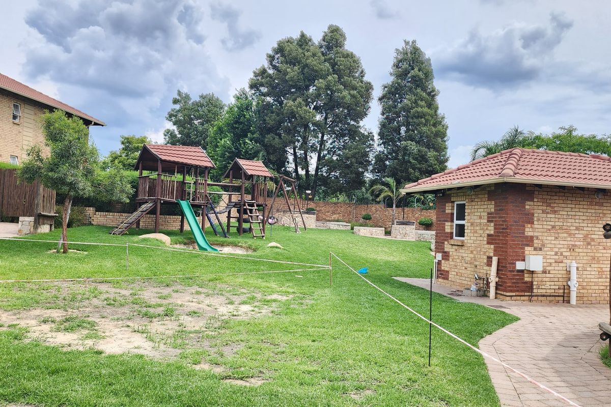 A spacious residential garden featuring a well-maintained lawn, a brick outbuilding with a tiled roof, and a paved walkway.