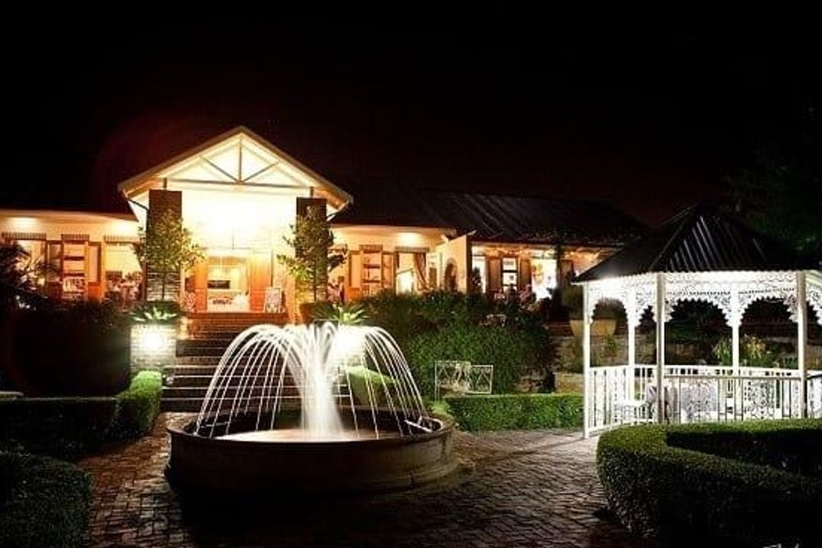 A beautifully illuminated rear garden area featuring a central stone fountain, a decorative gazebo, and manicured hedges set against the main building facade.