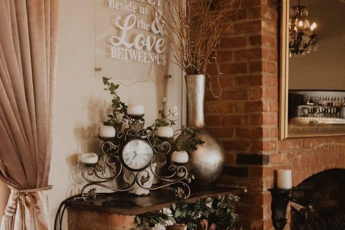 A cozy living area featuring a rustic exposed brick fireplace with integrated wood storage and classic tiled flooring.