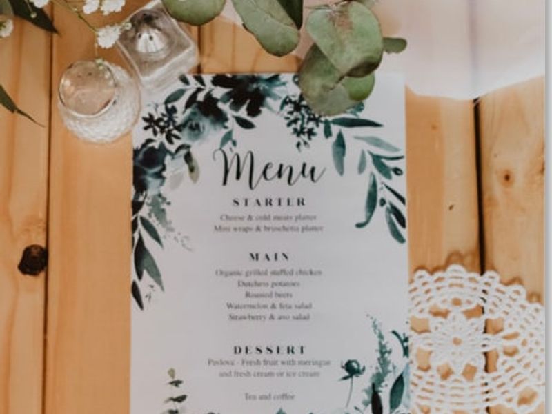 A close-up shot of a printed menu card placed on a wooden surface, decorated with floral elements and lace.