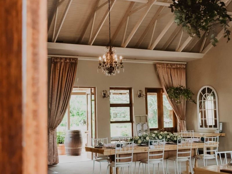 Spacious clubhouse interior featuring a high vaulted ceiling with exposed timber trusses, elegant chandelier lighting, and large windows providing natural light and garden access.