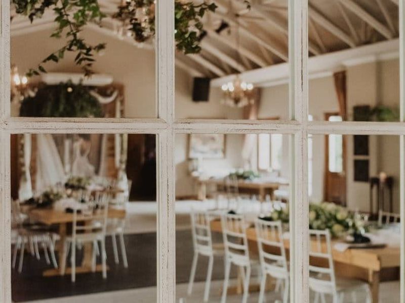 Spacious open-plan commercial venue featuring a high vaulted ceiling with exposed timber rafters, viewed through a decorative window-style mirror.
