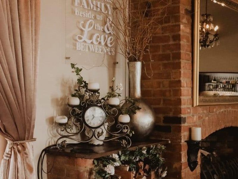 A cozy living area featuring a rustic exposed brick fireplace with integrated wood storage and classic tiled flooring.