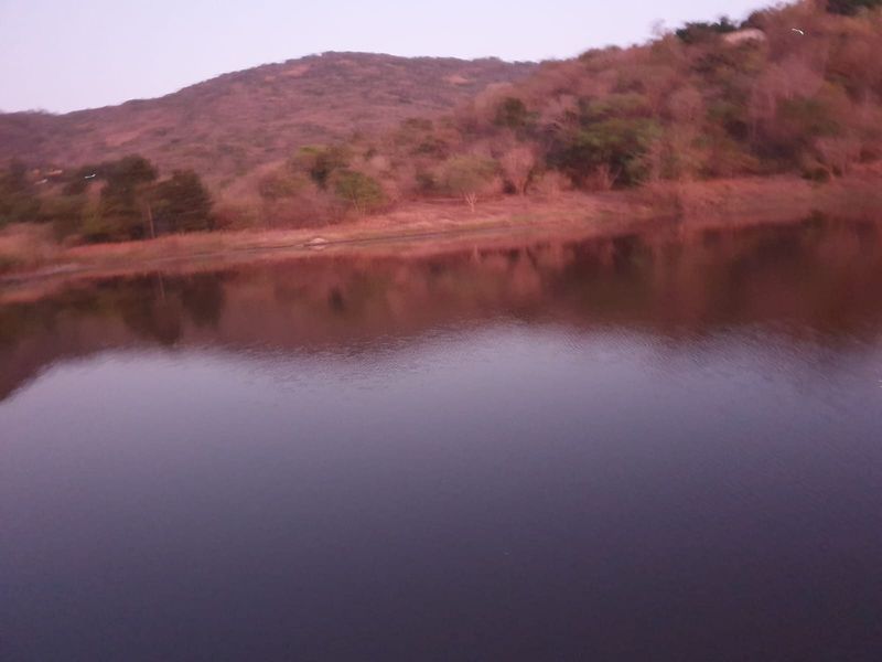A scenic view of a calm lake surrounded by hills and natural vegetation on the farm property.