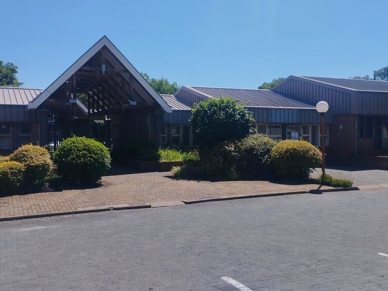 Front exterior view of a commercial office complex featuring a distinctive timber truss entrance, brick facade, and paved parking area.