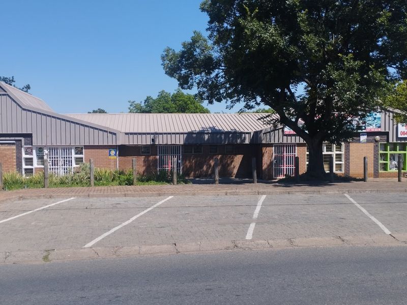 Front exterior view of a commercial property featuring a brick facade, metal roofing, and an adjacent paved parking area with security bollards.