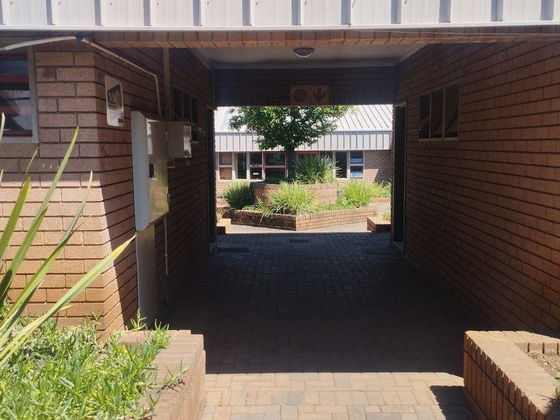 A covered brick-paved walkway connecting commercial building sections, featuring face brick walls and raised garden planters in the courtyard area.