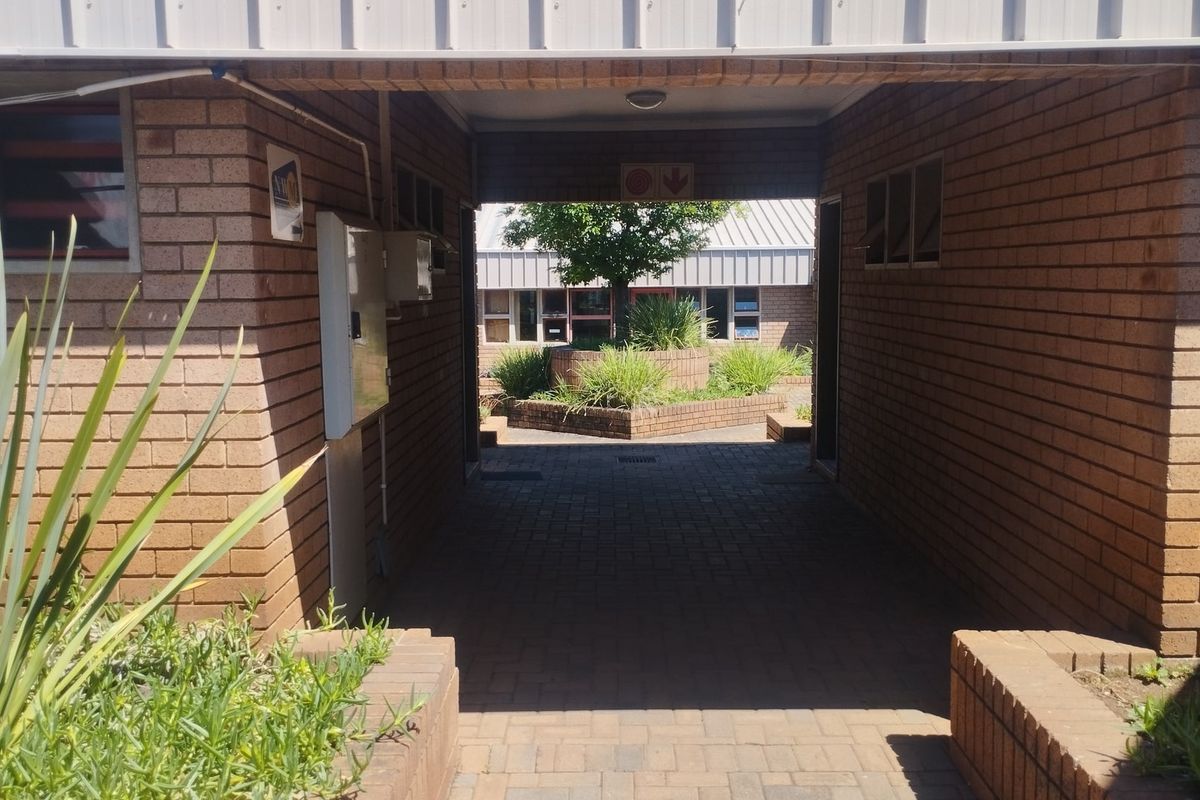 A covered brick-paved walkway connecting commercial building sections, featuring face brick walls and raised garden planters in the courtyard area.