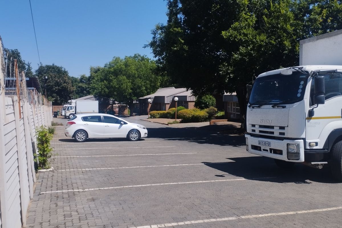 Commercial property exterior featuring a paved parking area, asphalt driveway, and secure boundary wall with razor wire fencing.