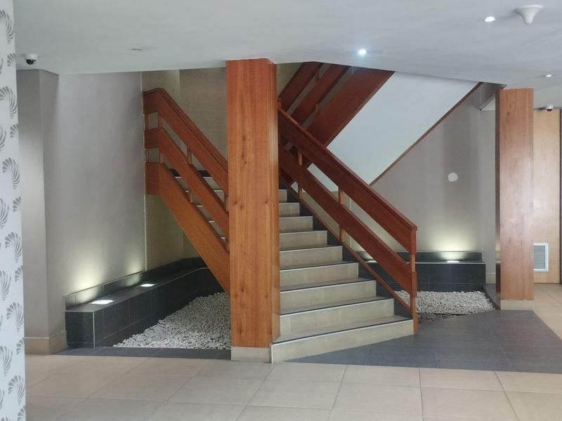 A modern commercial building entrance featuring a prominent wooden staircase, tiled flooring, and integrated decorative stone accents with recessed lighting.